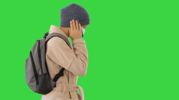Kvinna bär medicinsk mask promenader och ringa någon en telefonen på en grön skärm, Chroma Key. — Stockvideo
