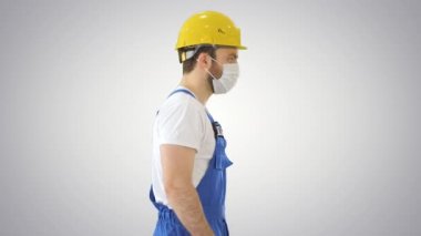 İnşaat işçisi sabit şapka ve maske takıyor ve arka planda yürüyor..