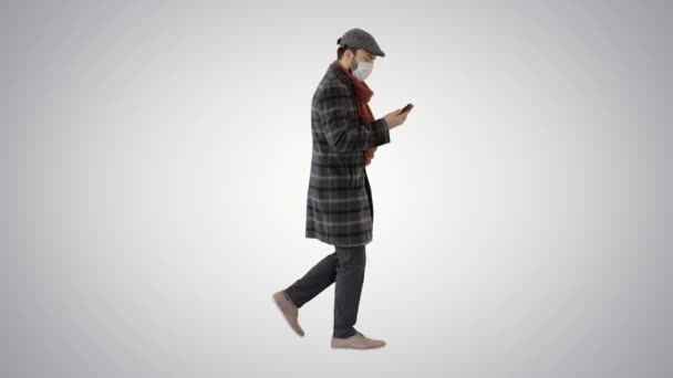 Felnőtt férfi visel védő orvosi maszk beszél a telefonon, és séta a gradiens háttér. — Stock videók