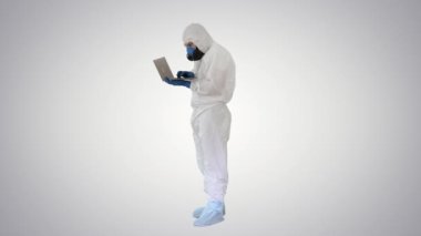 Beyaz koruyucu üniformalı bir doktor, gradyan arka planda dizüstü bilgisayar kullanıyor..