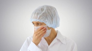 Diğerlerinin değişken arka planda enfeksiyon kapmasını önlemek için maskeli kadın doktor öksürüyor.