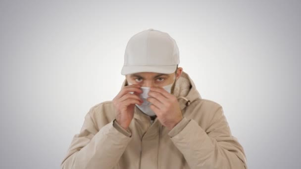 Man in warm coat walking and putting on medical mask on gradient background. — Stock Video