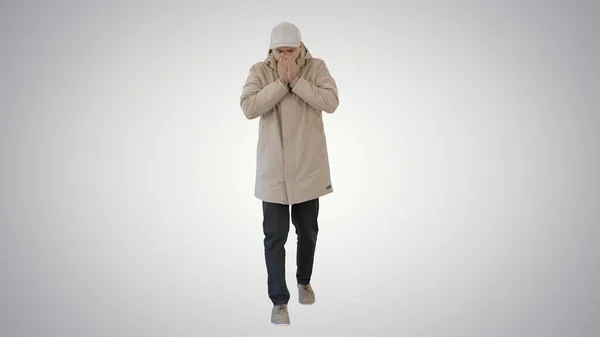 Человек в зимнем наряде ходит и кашляет на градиентном фоне . — стоковое фото