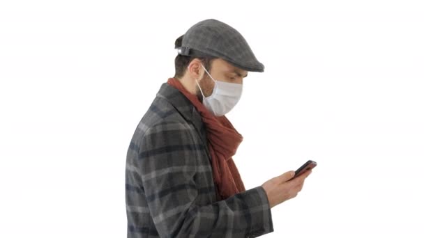 Dorosły mężczyzna nosi ochronną maskę medyczną, rozmawia przez telefon i chodzi po białym tle.. — Wideo stockowe