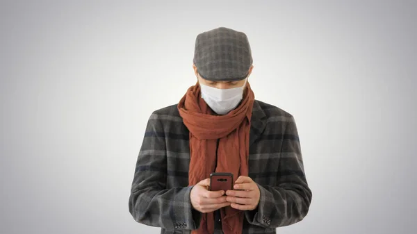 Dżentelmen w masce medycznej korzystający z telefonu i chodzący po gradientowym tle. — Zdjęcie stockowe