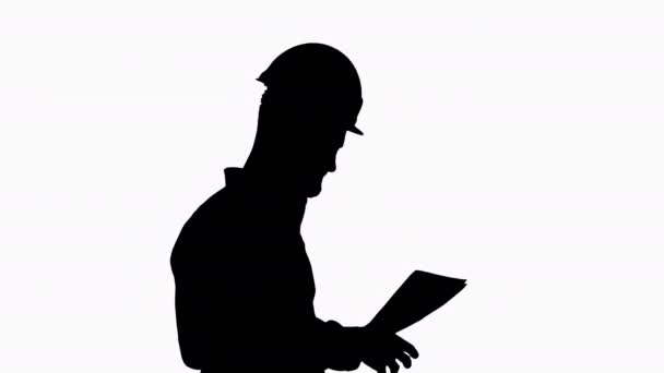 Silhouette Male engineer walking in a hard hat looking at documents. — Stock Video