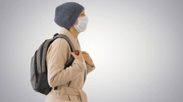 Профилактика вируса Covid-19, женщина в медицинской маске на лице ходит на градиентном фоне . — стоковое видео