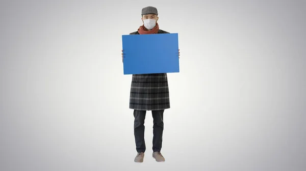 Hombre con un traje de moda y máscara médica sosteniendo pancarta en blanco sobre fondo degradado . — Foto de Stock