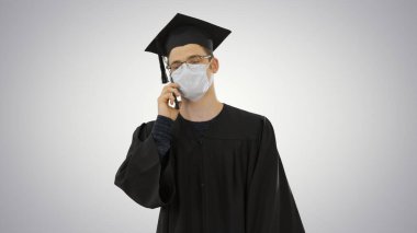 Genç bir lisansüstü öğrencisi, gradyan arka planda tıbbi maskeli akıllı telefonuyla arama yapıyor..
