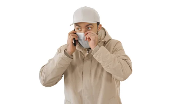 Europese jongeman bellen met een medisch masker op zijn gezicht op witte achtergrond. — Stockfoto