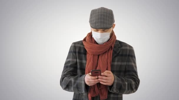 Cavalheiro em máscara médica usando telefone e andando em fundo gradiente . — Vídeo de Stock