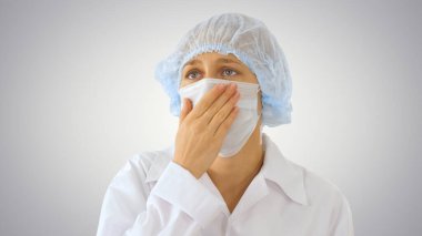 Diğerlerinin değişken arka planda enfeksiyon kapmasını önlemek için maskeli kadın doktor öksürüyor.