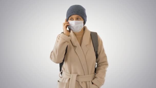 Meisje in een beschermend masker lopen en het maken van een telefoontje op de telefoon op gradiënt achtergrond. — Stockvideo