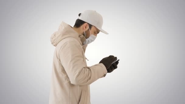 Uomo caucasico in maschera medica che cammina e usa il telefono su sfondo sfumato . — Video Stock