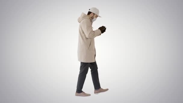 Caucasian man in a medical mask walking and using the phone on gradient background. — Stock Video