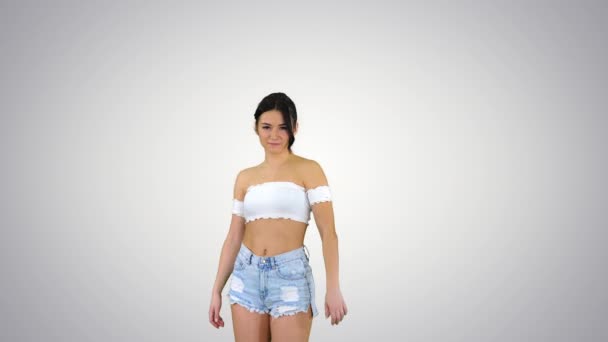 Urocza latynoska modelka w jeansowych spodenkach tańcząca na gradientowym tle. — Wideo stockowe