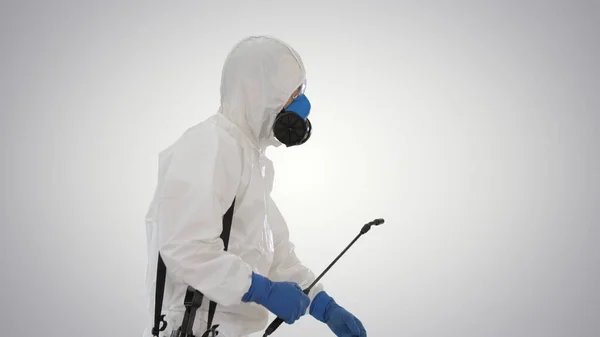 Pracovník v ochranných oděvech a obličejové masky chůze s dezinfekčním zařízením na gradientu pozadí. — Stock fotografie