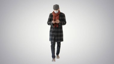 Tıbbi maskeli bir beyefendi telefon kullanıyor ve arka planda yürüyor..