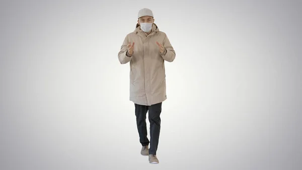 Man in winter outfit en medisch masker praten met u iets uit te leggen tijdens het lopen op gradiënt achtergrond. — Stockfoto