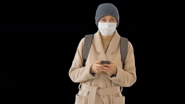 Žena oblečená v kabátě s lékařskou maskou pomocí telefonu a chůze, Alpha Channel — Stock video