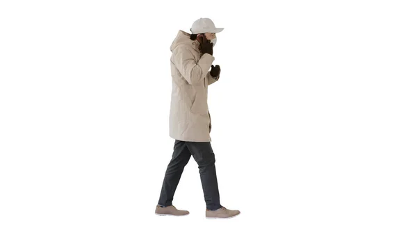 Man wears protective medical mask and talks on the phone walking on white background. — Stock Photo, Image