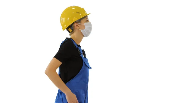 Vrouwelijke bouwvakker in overalls en in medisch masker lopend op witte achtergrond. — Stockfoto