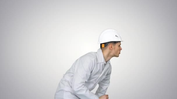 白い衣を着たヘルメットを着た若い労働者がグラデーションの背景で踊るのを楽しむ. — ストック動画