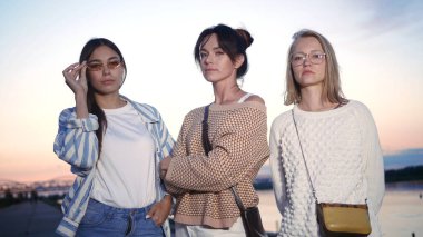 Üç ciddi kadın gün batımında kameraya bakar..