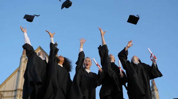 Groep afgestudeerden gooien hun caps vrolijk in de lucht. — Stockfoto