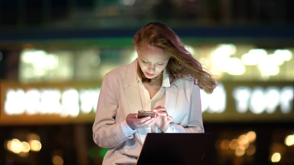 Młoda piękna kobieta za pomocą smartfona siedzi z laptopem — Zdjęcie stockowe