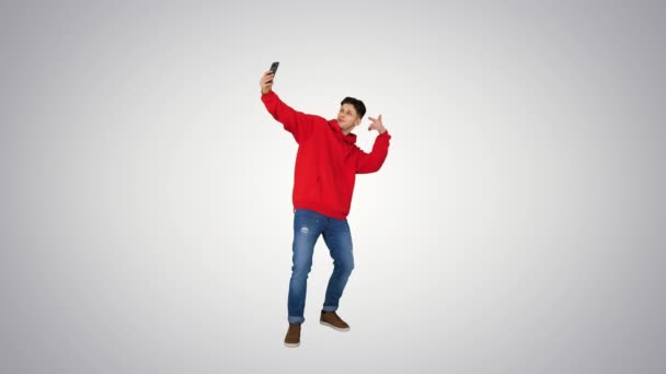Emocionado hombre casual bailando y haciendo selfie con su teléfono en el fondo gradiente . — Vídeo de stock