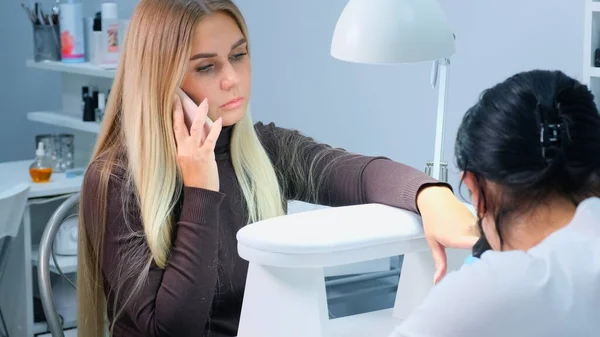 Manucure fait manucure pour une femme dans un salon de beauté. Une femme blonde parle au téléphone pendant une manucure . — Photo