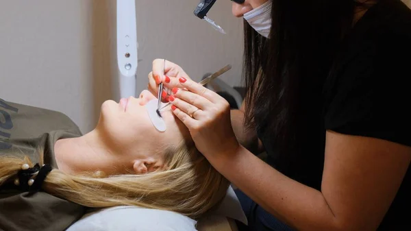 Olho de mulher com pestanas longas. Extensão das pestanas. Lashes, close up, foco selecionado. Colando pestanas artificiais com pinças. Esteticista em lupa óculos executa pequeno trabalho laborioso . — Fotografia de Stock