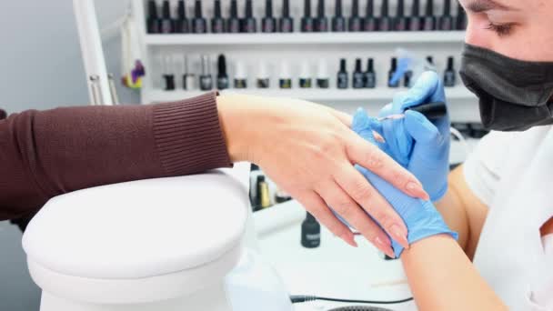 Manikiurzystka nakłada lakier żelowy na paznokcie klienta w salonie kosmetycznym. Zbierzcie gwoździe. Manicure — Wideo stockowe