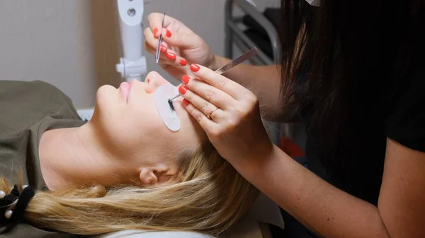 Master vergrößert große Wimpern für eine Kundin im Schönheitssalon. Wimpernverlängerung. — Stockfoto