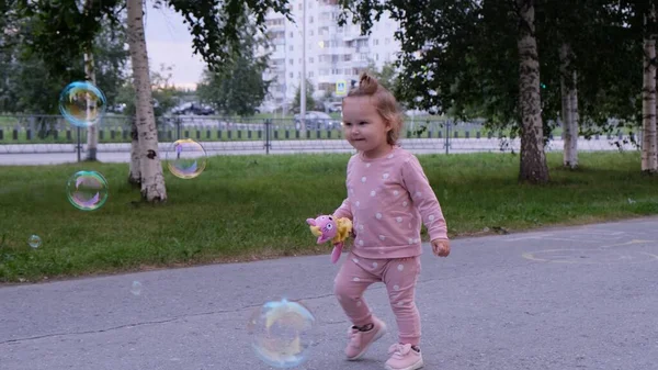 Šťastná holčička běží na mýdlové bubliny v letním parku. Šťastné dětství. — Stock fotografie