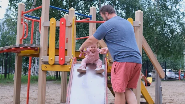 Vader en dochter spelen in de Speeltuin, een man vangt een dochter die naar beneden beweegt van een Childrens glijbaan. — Stockfoto