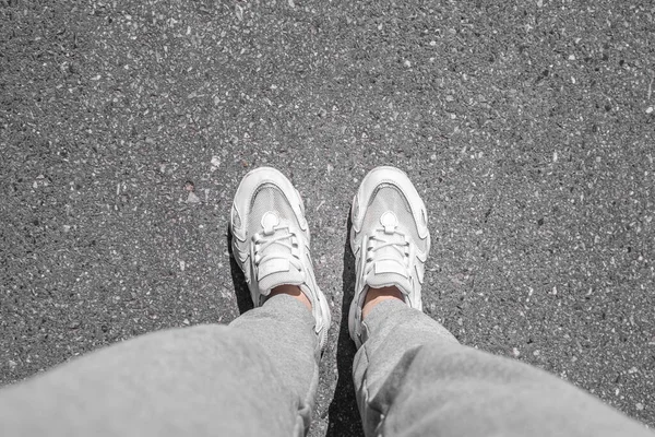 Betonun üzerinde yürüyen beyaz spor ayakkabılar. Kaldırımda spor ayakkabılar. Asfalttaki bacakların üst görünümü. — Stok fotoğraf