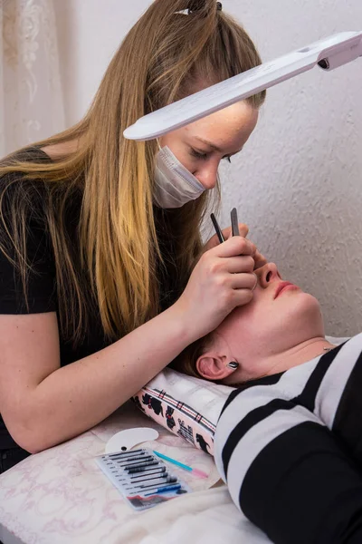 Salon de beauté. gros plan, procédure d'extension des cils. Le maître colle chaque cilium avec une colle spéciale, fonctionne à l'aide de deux pinces à épiler — Photo