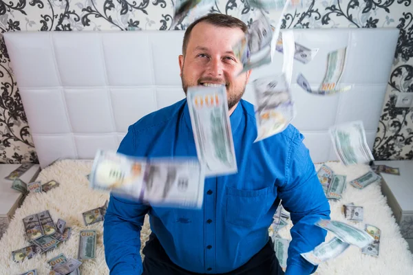 Чоловік насолоджується величезним багатством. чоловік кидає багато банкнот на біле ліжко, кидає гроші — стокове фото
