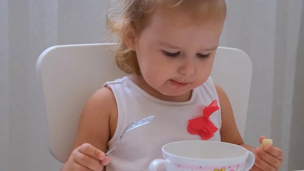 Zuigeling meisje eten baby eten aan een kleine Kinder tafel op een witte achtergrond. Voeding en voeding van kinderen. — Stockfoto