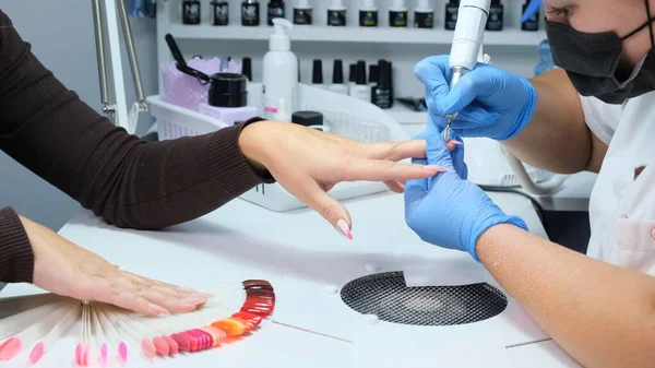 Zamknij drzwi. Elektryczne wiertarki do paznokci w salonie manicure. Manicure sprzętowy w salonie piękności. Manikiurzystka usuwa stary żel z paznokci klientów. Grill ssący. Proces manicure paznokci w salonie piękności. — Zdjęcie stockowe