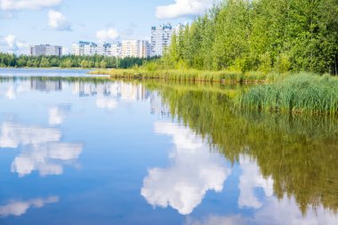Küçük bir göl ve şehrin güzel manzarası. Gölde hafif bir rüzgar. Bulutlar suya yansıyor.