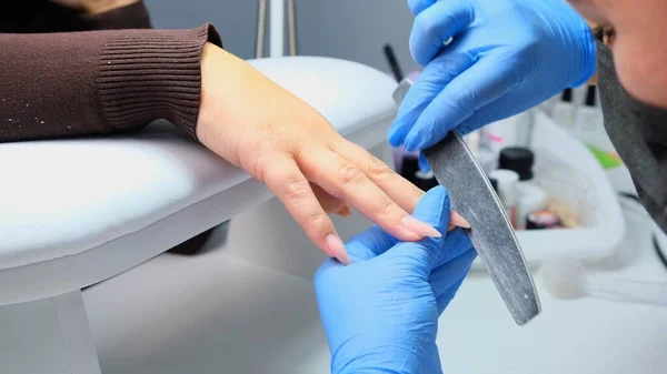 A manicura arquiva um prego com uma lima do prego a um cliente. Processo de manicure, extensão das unhas. close-up — Fotografia de Stock