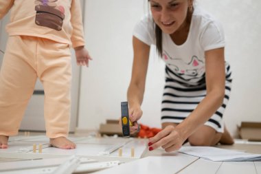 Anne ve kızı bir kutu toplar. Bir kadın tornavida kullanarak beyaz ahşap bir dolap montajı olduğunu.