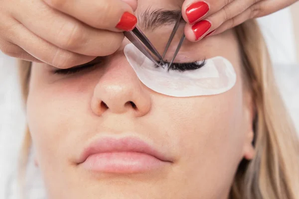 Eyelash Extension Procedure. Woman Eye with Long false Eyelashes. Closeup macro shot of fashion eyes in beauty salon. Hands beautician. — ストック写真