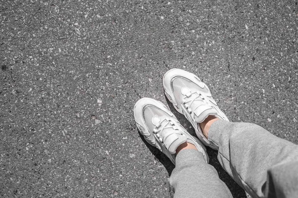 Λευκά αθλητικά παπούτσια που περπατούν στο τσιμέντο. Αθλητικά παπούτσια στο πεζοδρόμιο. Κάτοψη των ποδιών στην άσφαλτο. — Φωτογραφία Αρχείου