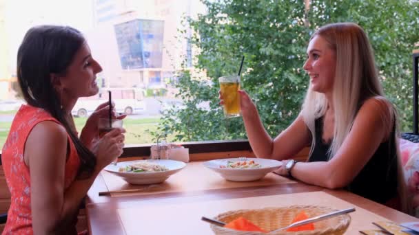 Дві модні круті дівчата, друзі, блондинка і брюнетка п'ють коктейлі в кафе . — стокове відео