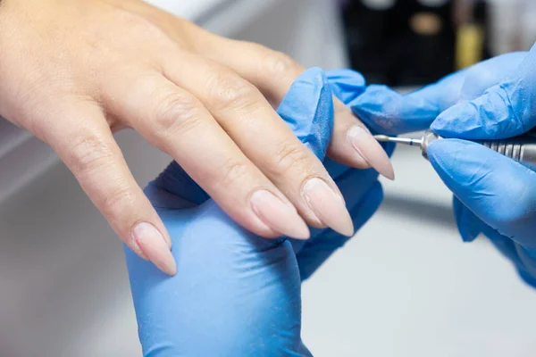 Closeup shot of hardware manicure in a beauty salon. Manicurist is applying electric nail file drill to manicure on female fingers