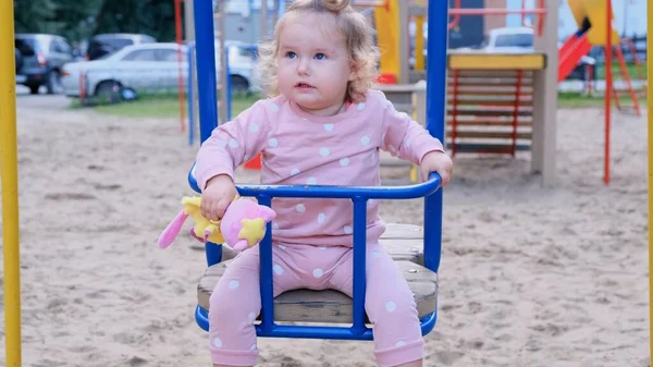Nizjnevartovsk, Rusland - 25 augustus 2019: klein meisje 2 jaar oud die op een zomerherfstdag schommelt op een schommel in de speeltuin. — Stockfoto